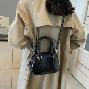 Detail showing a stylish black glossy PU leather handbag worn as a crossbody shoulder bag
