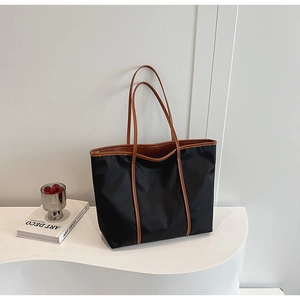 Elegant black nylon tote bag with brown leather handles displayed on a modern white stand