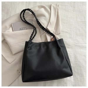 Minimalist black pebble leather tote bag with woven straps and amber buckles on a blazer