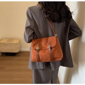 Detailed view of the brown suede messenger bag worn by a model in a dark gray suit
