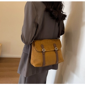 Detail view of mustard yellow velvet messenger bag with brown straps on gray blazer