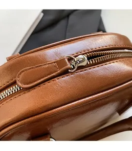 Close-up of smooth gold-tone metal zipper on a caramel brown leather shoulder bag