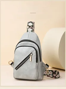 Detail of grey crossbody bag featuring a geometric strap and gold metal hardware