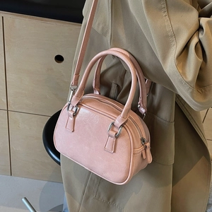 Detail view of pink PU leather Boston bag with shoulder strap worn over a beige trench coat