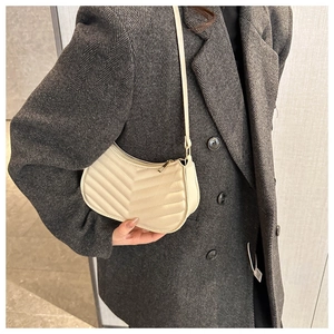 Detail of a creamy crescent shoulder bag with chevron quilting worn on a grey suit jacket