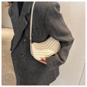 Detail view of cream chevron quilted PU leather shoulder bag on a grey textured blazer background