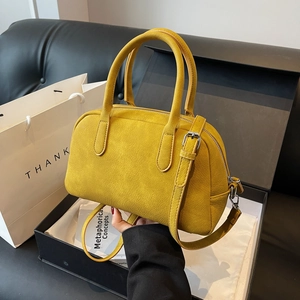 Detail showing matte ginger yellow Boston bag with silver buckle strap inside a gift box