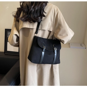Close-up of black crossbody bag with silver buckles worn with a beige trench coat