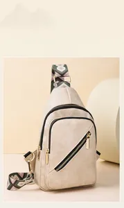 Detail view of beige crossbody bag with textured fabric, gold zippers and geometric strap
