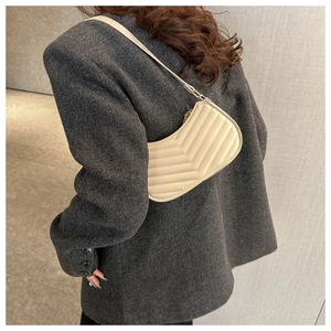 Detail of cream-white V-quilted shoulder bag with thin strap on grey blazer