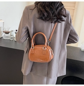 Close-up of a brown PU leather Boston bag shown on a model in a minimal cafe setting