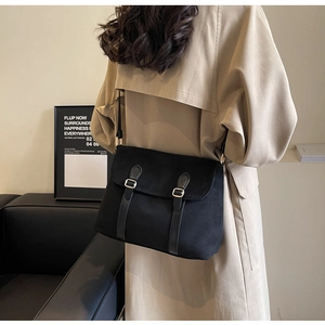 Detailed view of a black suede messenger bag with gold buckles worn by a model in a trench coat