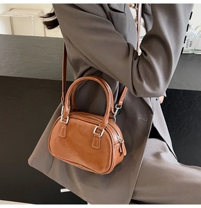 Detail view of a brown faux leather Boston handbag worn by a model in a gray suit