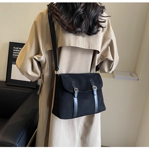 Detail of a black suede crossbody bag with leather straps on a fashion model