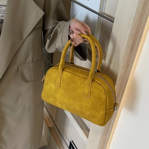 Close-up of yellow suede Boston handbag with dual handles and smooth metallic zipper