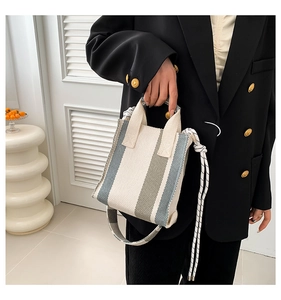 Detail of striped canvas handbag with rope strap on model wearing a black blazer
