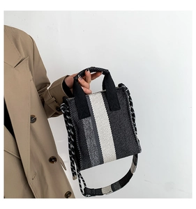 Detail of woven canvas striped handbag featuring wide printed strap and knotted drawstrings