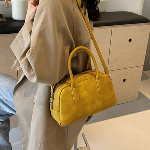 Detailed close-up of a bright yellow suede-like Boston bag with dual handles and silver clips