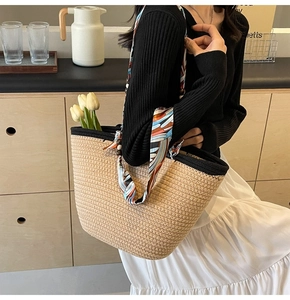 Detail of woven straw tote bag featuring contrast trim and decorative floral silk scarf handle