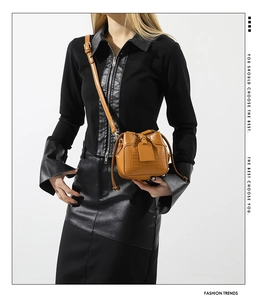 Detail view of brown crocodile texture bucket bag worn by model over black outfit