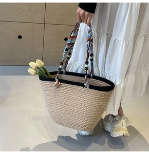 Detail of woven straw tote bag with black trim and colorful silk scarf wrapped handle