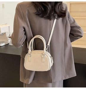 Close-up of beige dome handbag styled as a crossbody bag in a warm cafe setting