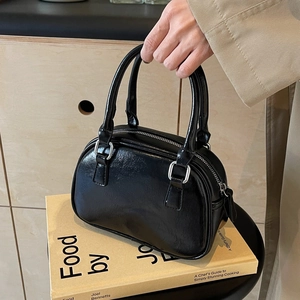 Chic black glossy leather Boston handbag with silver hardware displayed on a wooden shelf