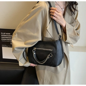 Detail of black pebbled leather crossbody bag featuring gold chain and front zipper pocket