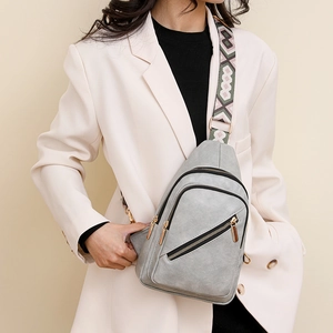 Close-up of grey textured leather crossbody bag with patterned wide woven strap on model