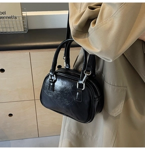 Detail of elegant black glossy PU leather boston bag worn with a stylish trench coat