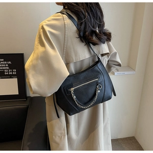 Detail of black pebbled leather crossbody bag featuring a stylish gold chain accent