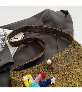 Close-up of golden woven crossbody bag with colorful charms and decorative pearl button detail