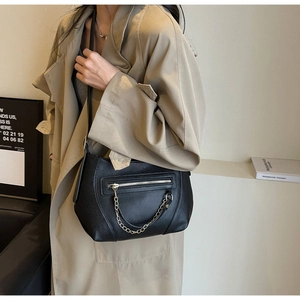 Close-up of black litchi pattern leather crossbody bag with silver chain detail on model