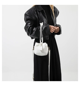 Detail of white crocodile embossed bucket bag with drawstring closure and golden hardware