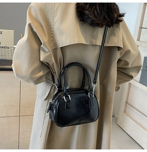 Close-up of black patent leather round bag with silver hardware on khaki coat
