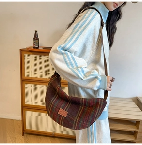 Detail of red and green plaid woolen crescent bag with leather brand patch on front