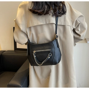 Detail of black pebbled leather crossbody bag with chain on a beige trench coat