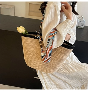Detail of woven straw tote bag with black trim and decorative silk scarf accessory