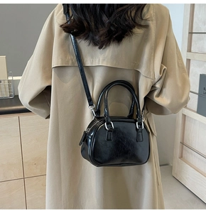 Detailed view of a black glossy crossbody bag worn with a stylish beige trench coat