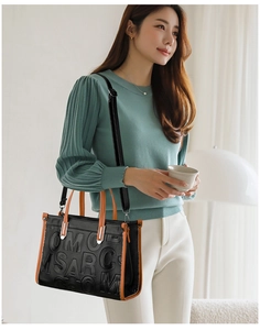 Détail d'un sac bandoulière noir avec lettres gaufrées et poignées orange contrastées
