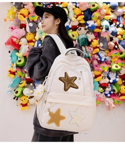 Side view of white canvas backpack featuring plush star patches and a hanging mascot toy