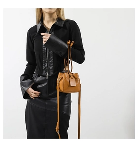 Detailed view of tan crocodile pattern mini bucket bag worn by model over black jacket