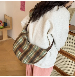 Detail of green plaid tweed half-moon crossbody bag with leather logo patch and strap