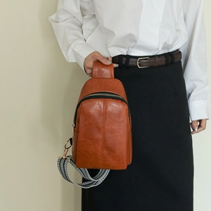 Brown vintage faux leather crossbody bag with geometric woven strap on a white shirt