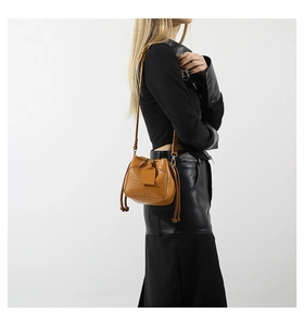 Brown crocodile pattern bucket bag with tassel drawstring shown on a model's shoulder