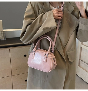 Pink glossy faux leather Boston bag with crossbody strap worn by a model in a trench coat
