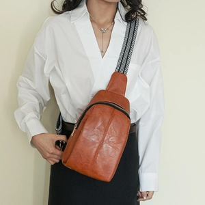 Detail of orange leather crossbody bag featuring geometric patterned wide textile strap