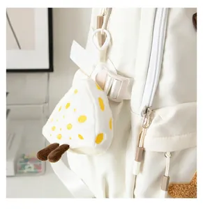 Close-up of a cute plush cheese pendant with yellow spots hanging on a white canvas backpack