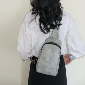 Grey textured leather crossbody bag with geometric woven strap shown on a model
