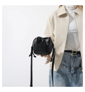 Detail of black crocodile texture bucket bag with drawstring closure and gold hardware
